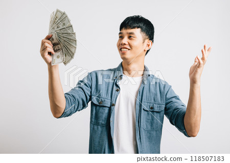 Portrait smiling Asian young man holding a bunch of money and pointing studio shot isolated white background, happiness and excitement man in dollar banknotes celebrating his financial success 118507183
