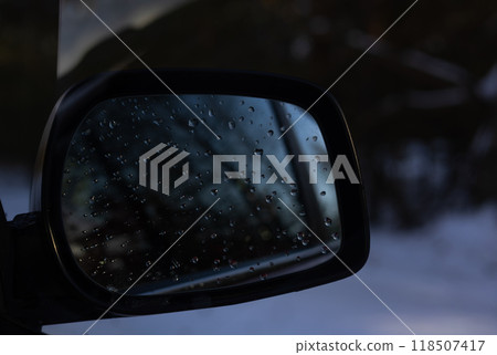 The car mirror reflects a serene winter landscape with water droplets, adding unearthly beauty to the tranquil scene. Fairytale winter forest reflected in the car mirror. The car mirror reflects a serene winter landscape with water droplets, adding unearthly beauty to the tranquil scene. Fairytale winter forest reflected in the car mirror. 118507417