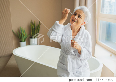 Woman applying natural drops cosmetics oil to face skin. Mature adult old woman applying nourishing anti age serum with pipette doing daily beauty routine. Senior woman gets kin scare facial treatment 118508509