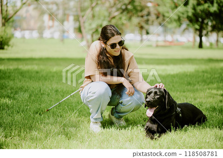 Young brunette woman with disability petting her lovely black Labrador while he lying on grass and resting Young brunette woman with disability petting her lovely black Labrador while he lying on grass and resting 118508781