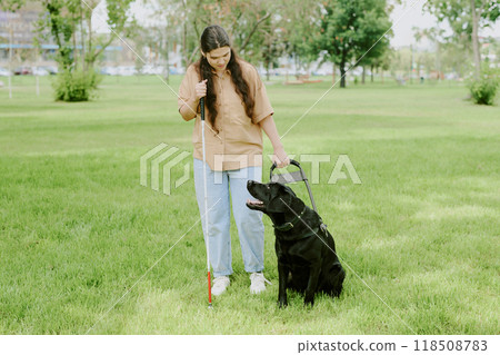 Brunette woman holding metal cane and guide dog leash while her black Labrador looking at her 118508783