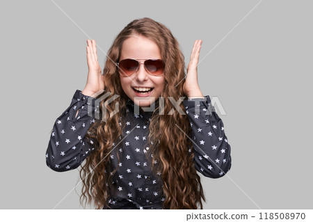 Joyful young girl laughing with long curly hair and sunglasses on gray 118508970