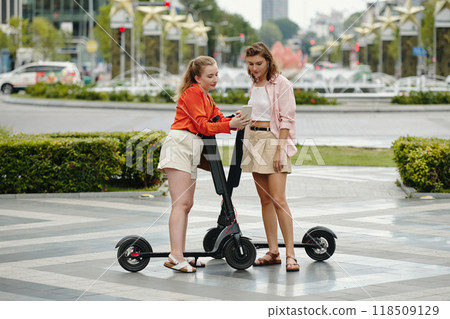 Pair of Women Riding Electric Scooters in Urban Environment 118509129