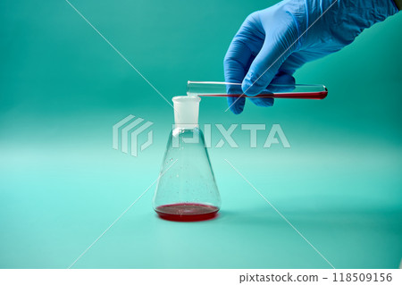 Scientist pouring red liquid into conical flask during experiment Scientist pouring red liquid into conical flask during experiment 118509156