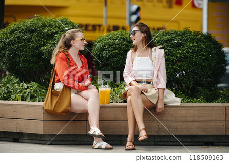 Friends Enjoying Beverages While Sitting on Bench Outdoors Friends Enjoying Beverages While Sitting on Bench Outdoors 118509163