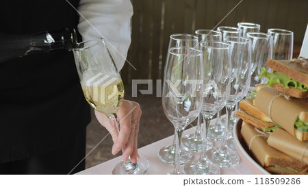 A woman pours champagne into a glass, close-up. Catering with sandwiches. 118509286
