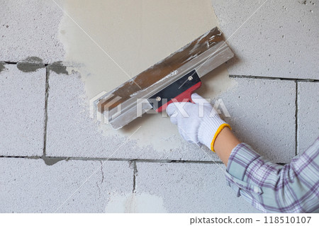 The master levels the wall with a spatula. The master levels the wall with a spatula. 118510107