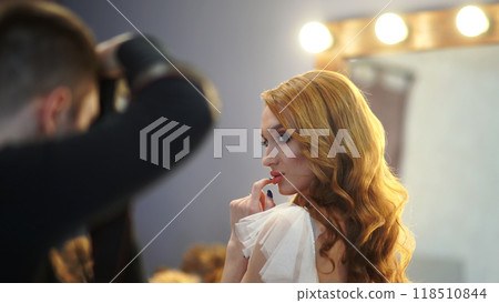 Hairstylist is styling the long wavy hair of a stunning bride in a white gown at a salon Hairstylist is styling the long wavy hair of a stunning bride in a white gown at a salon 118510844