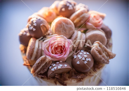 Decorating a scrumptious birthday cake with chocolate, macarons, a pink rose, and chocolate shavings Decorating a scrumptious birthday cake with chocolate, macarons, a pink rose, and chocolate shavings 118510846