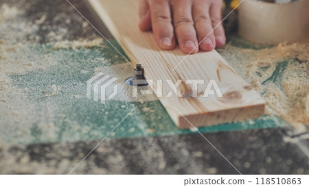 Close up of a carpenter working wood plank using electric milling machine in workshop Close up of a carpenter working wood plank using electric milling machine in workshop 118510863