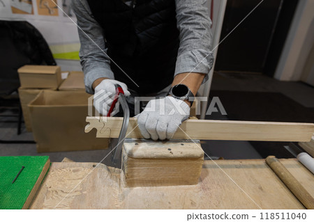 male hands in work gloves sawing wooden blank with thin hand saw 118511040