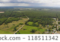 Aerial drone view of expansive woodland and a winding road leading to a quaint village on a cloudy summer day 118511342