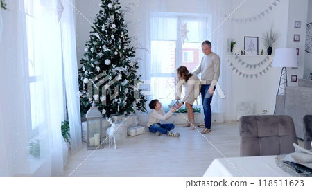 Parents stand by Christmas tree hand their son special gift magic and excitement of holiday traditions. Twinkling Christmas tree father and mother present son with Christmas gift sharing in happiness. 118511623