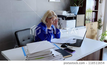 Businesswoman in suit visibly tired sits in office with head resting on hand emotional strain burnout. Sitting at office desk mid adult businesswoman in attire holds head overwork work-life balance. Businesswoman in suit visibly tired sits in office with head resting on hand emotional strain burnout. Sitting at office desk mid adult businesswoman in attire holds head overwork work-life balance. 118511654