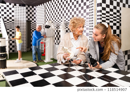 Grandmother with tweenager granddaughter trying to find solution of conundrum in lost room designed as chess board 118514907