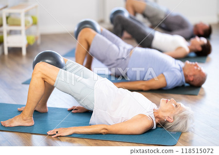 Group of mature women and men practicing pilates with soft ball in fitness studio 118515072