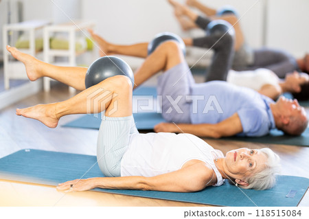 Group of mature women and men practicing pilates with soft ball in fitness studio Group of mature women and men practicing pilates with soft ball in fitness studio 118515084