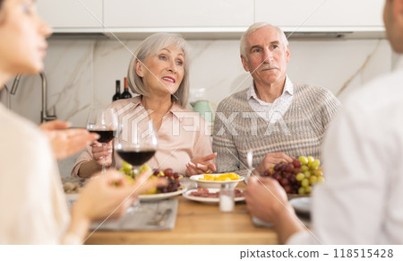 Mature married couple are sitting at table, enjoying food and wine with middle-aged guests. Mature married couple are sitting at table, enjoying food and wine with middle-aged guests. 118515428