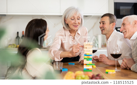 Joyful senior parents and young couple sitting around table playing brick game Joyful senior parents and young couple sitting around table playing brick game 118515525