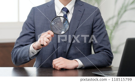 Businessman raising a magnifying glass to his chest 118515799