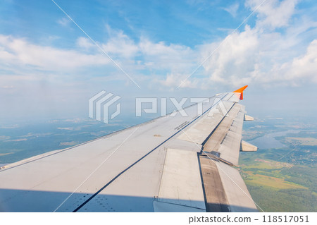 View of airplane wing, blue skies and green land during landing. Airplane window view. 118517051