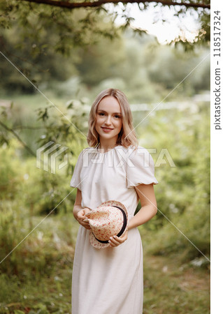 Woman standing in park holding straw hat.  118517324