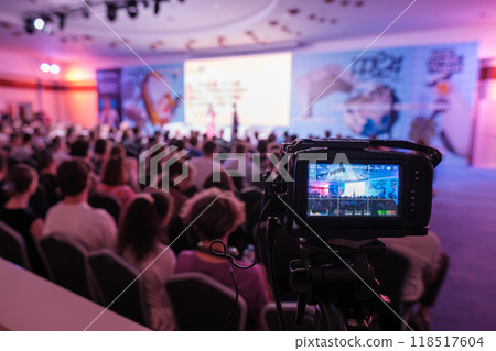 Professional video camera recording conference with audience in background Professional video camera recording conference with audience in background 118517604