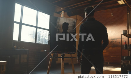 Artist admiring a silhouette painting in a sunlit studio 118517772