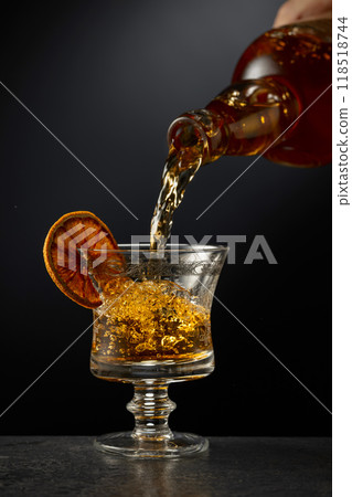 Rum or whiskey is poured from a bottle into a glass. Rum or whiskey is poured from a bottle into a glass. 118518744