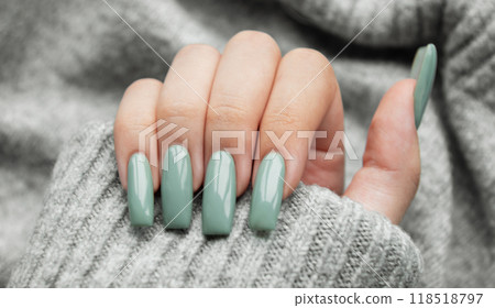 Elegant hand with long, mint-green nails resting on a cozy gray sweater 118518797