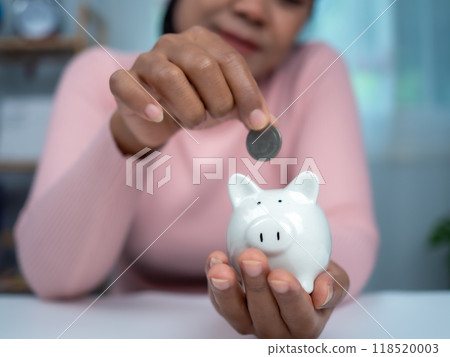 Woman wearing a pink shirt put coins in the piggy bank for saving money and financial concept, Business banking and financial concept, Saving money for retirement funds and insurance concept. 118520003