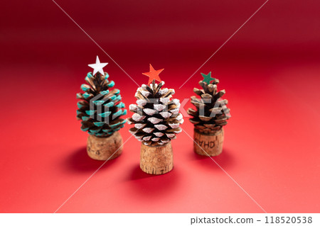Creative natural decorations, pine cone Christmas trees on cork bases, white, orange, green stars, eco friendly holiday decor, festive craft, red background, 118520538