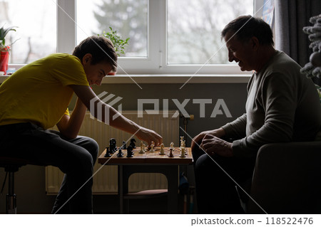 Young teenage boy and older man enjoying a chess game indoors during daylight hours 118522476