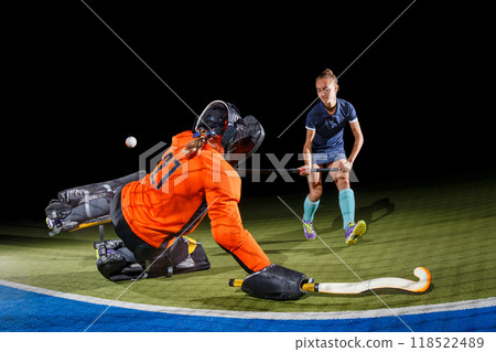 Intense field hockey action between goalkeeper and forward against black background 118522489