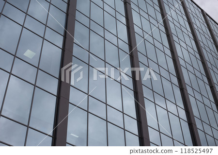 Glass facade of building goes up into the gray gloomy sky, cloudy sad day for routine work in office 118525497