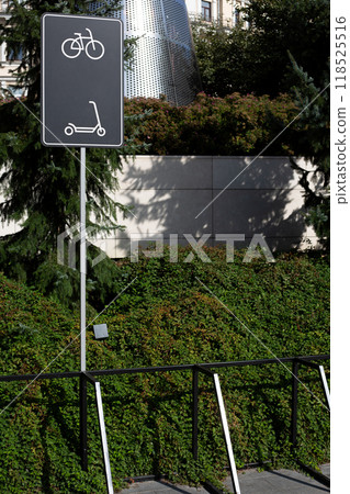 Special area with metal structure for securing bicycles and scooters in park next to sign indicating the parking area for personal mobile vehicles with locker Special area with metal structure for securing bicycles and scooters in park next to sign indicating the parking area for personal mobile vehicles with locker 118525516