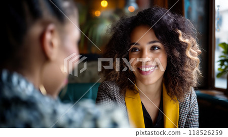 Two women engaging in a friendly conversation at a cozy cafe during the afternoon surrounded by warm natural light 118526259