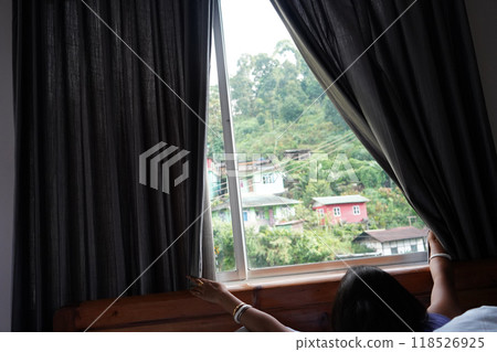 Young tourist slide curtain to take view of Moutain from window at Lingtham east Sikkim Young tourist slide curtain to take view of Moutain from window at Lingtham east Sikkim 118526925