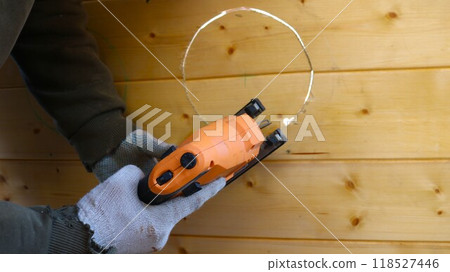 working with a jigsaw on a wooden surface, cutting a circle with a jigsaw, a working construction tool in male hands in gloves close-up during decorative woodworking working with a jigsaw on a wooden surface, cutting a circle with a jigsaw, a working construction tool in male hands in gloves close-up during decorative woodworking 118527446