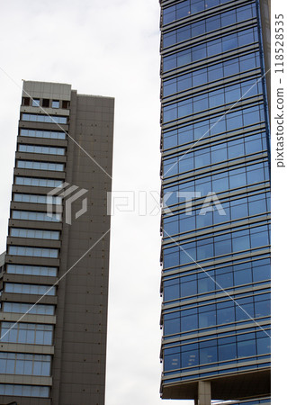 Vertical photography of two skyscrapers, tall glass buildings with balconies against sky, facade of multi storey buildings with blue glass Vertical photography of two skyscrapers, tall glass buildings with balconies against sky, facade of multi storey buildings with blue glass 118528535