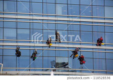 Climbers clean the glass facade of skyscraper, hard work at height, workers in overalls wash windows of building, climbers on ropes descending modern house 118528536