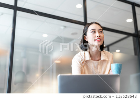 A woman looking at her business partner while drinking coffee between computer tasks A woman looking at her business partner while drinking coffee between computer tasks 118528648