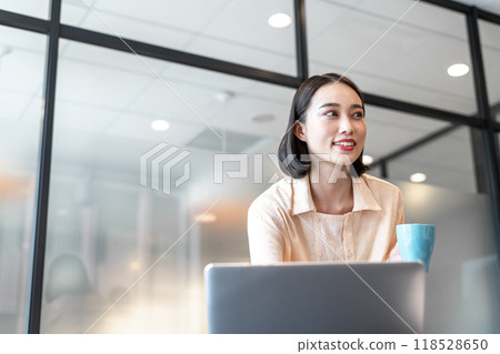 A woman looking at her business partner while drinking coffee between computer tasks A woman looking at her business partner while drinking coffee between computer tasks 118528650