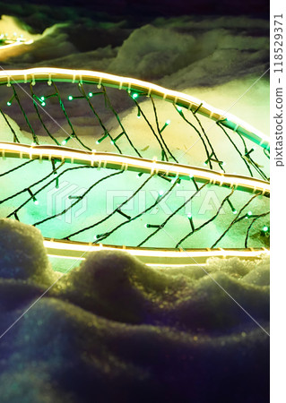 New Year LED garland in the form of a tree leaf on snow. Festive vertical template, holiday background with copy space. Neon decorative lighting in winter. 118529371