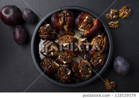 Plums baked with Camembert cheese, walnuts and honey on a black plate. Popular hot appetizer. Selective focus, close-up. Plums baked with Camembert cheese, walnuts and honey on a black plate. Popular hot appetizer. Selective focus, close-up. 118529579