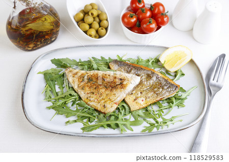 Fried dorado fillet with crispy skin. Arugula, cherry tomatoes, olives, lemon and olive oil. Traditional Mediterranean dish. White background. Selective focus, close-up. 118529583