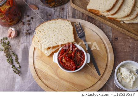 Sun-dried tomatoes in olive oil on a round board with homemade bread and cottage cheese in a rustic style. Traditional home cooking. Selective focus, close-up. Sun-dried tomatoes in olive oil on a round board with homemade bread and cottage cheese in a rustic style. Traditional home cooking. Selective focus, close-up. 118529587