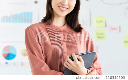 Smiling businesswoman holding a tablet in front of a whiteboard 118530303