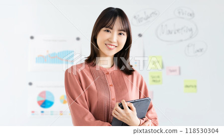 Smiling businesswoman holding a tablet in front of a whiteboard 118530304