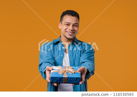Stylish Excited Man Holding Gift Box And Gives It By Hands To Camera on Yellow. Stylish Excited Man Holding Gift Box And Gives It By Hands To Camera on Yellow. 118530565